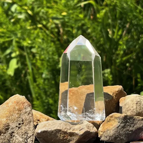 Hand holding clear quartz in sunlight casting rainbow patterns